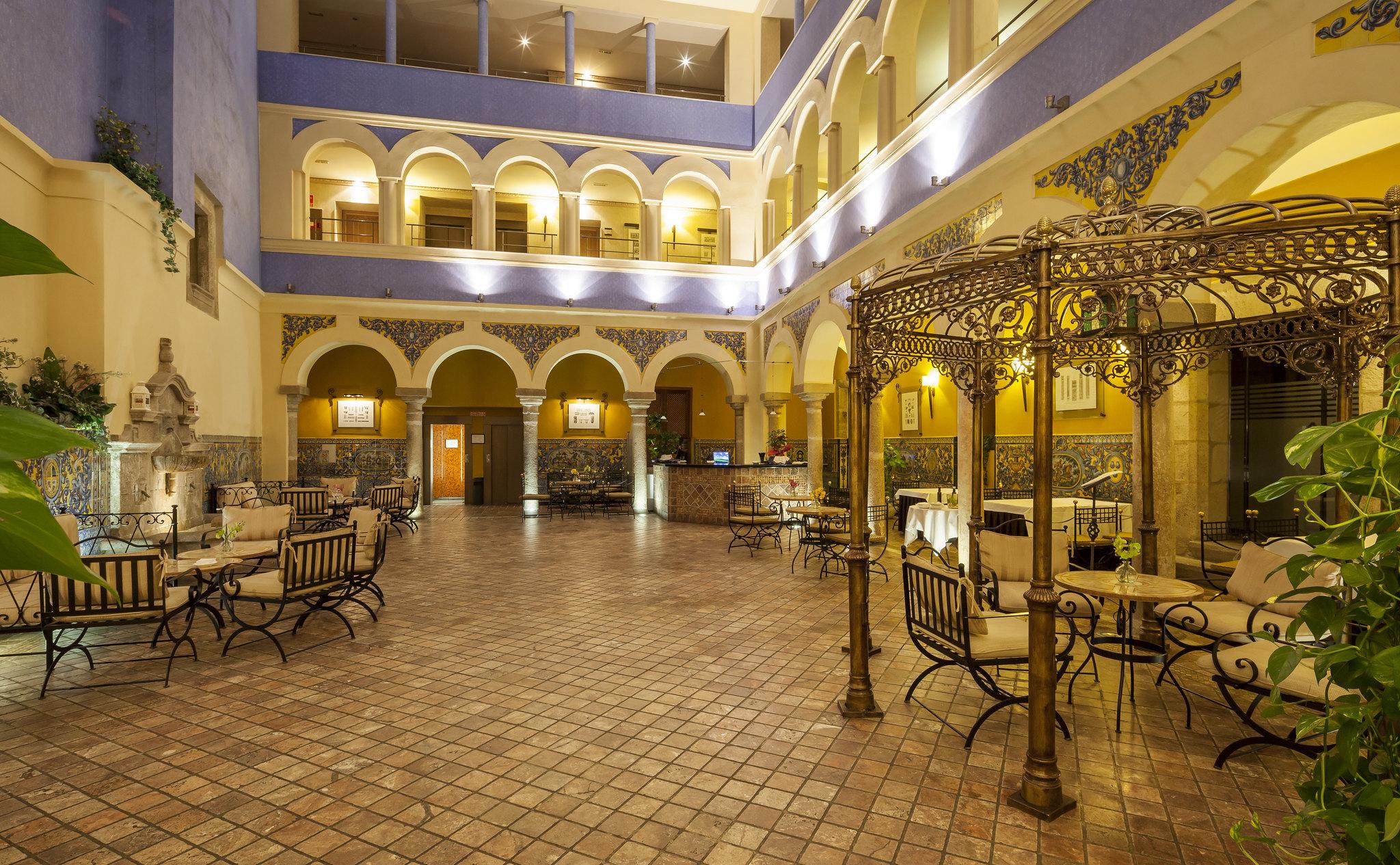 伊露尼翁梅里达宫酒店 外观 照片 The photo shows an elegant indoor space, likely a hotel or a courtyard. The architecture features arched openings supported by columns, with a warm color palette that includes soft yellows and blues. The flooring is made of patterned tiles, and there