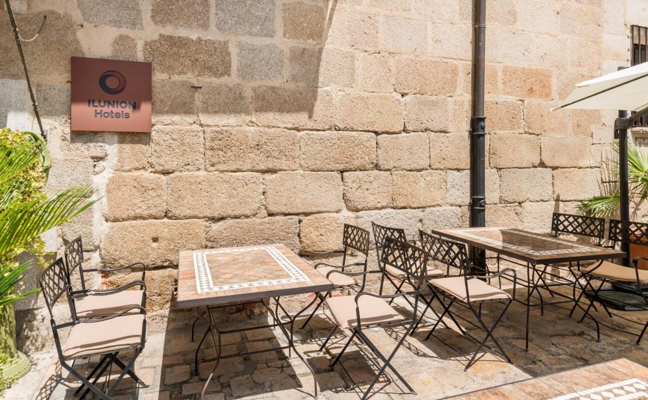 伊露尼翁梅里达宫酒店 外观 照片 The photo shows an outdoor seating area with several metal chairs and tables, arranged in a casual setting. The tables feature a decorative design, and there is a sign for a hotel named "Ilunion Hotels" visible on the wall. The background consists of